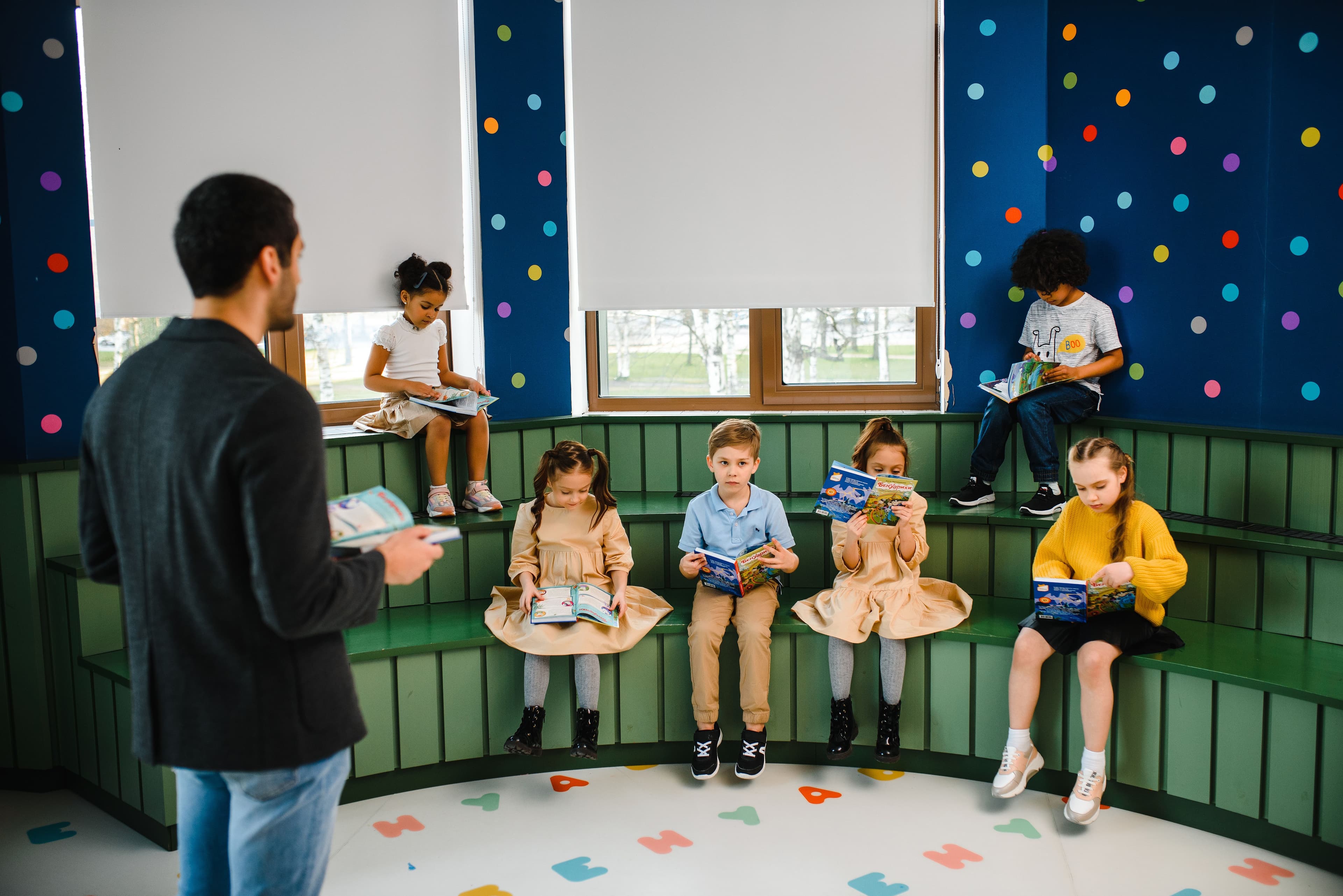 A teacher holding a picture book while a group of primary-age pupils read in a colourful classroom