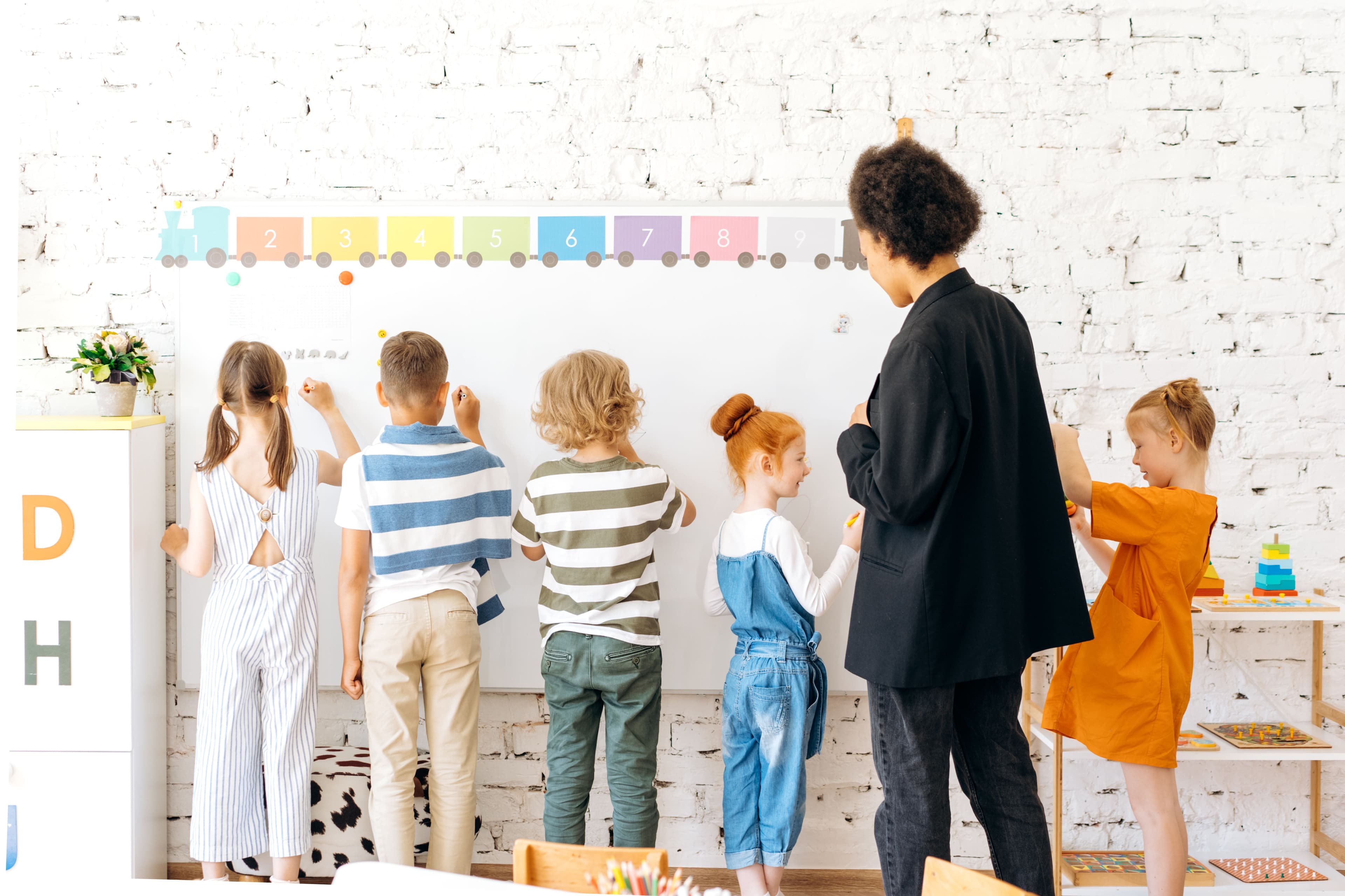 Primary-age pupils creating together on a classroom whiteboard with support from their teacher
