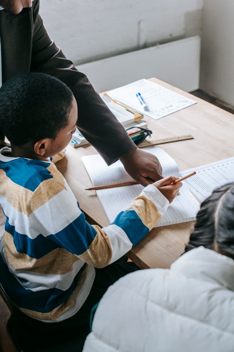 A teacher supporting primary-age pupils as they work together on classroom activity sheets